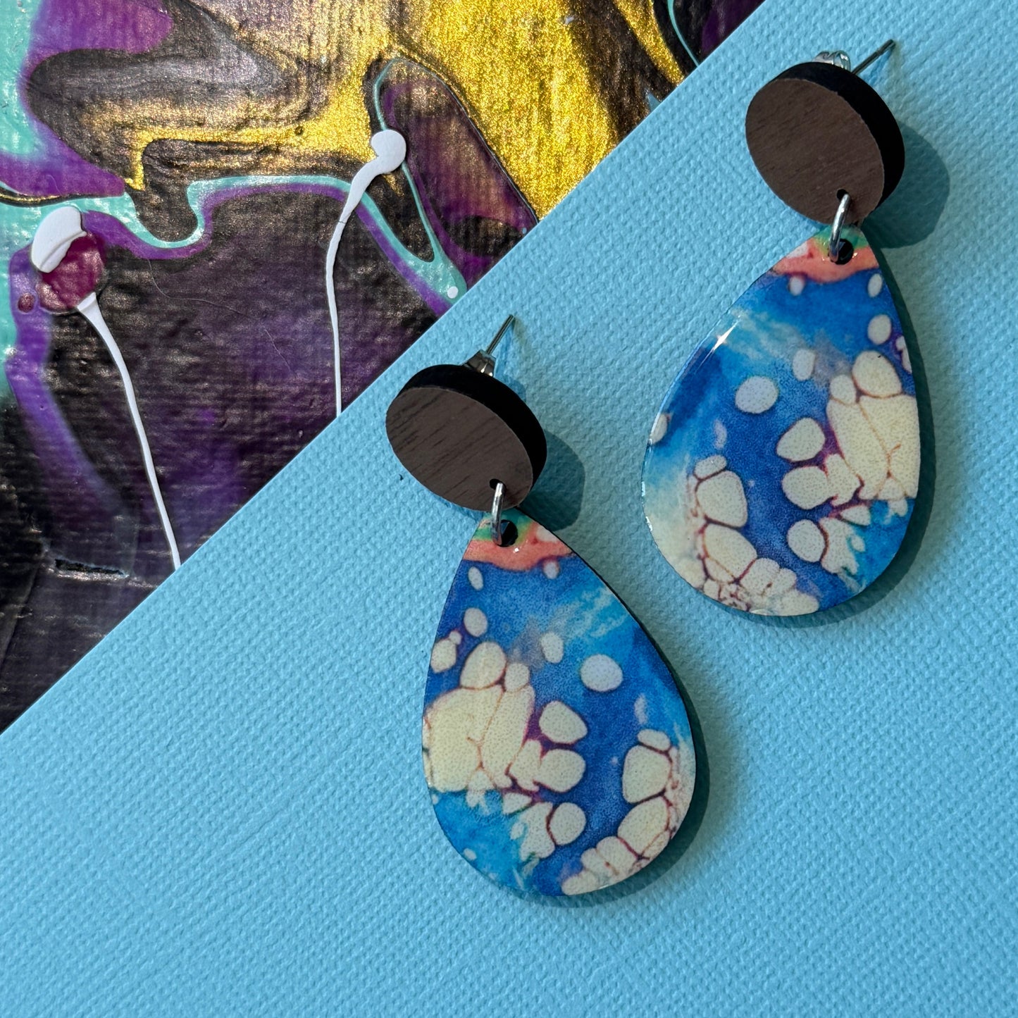 Colorful abstract teardrop earrings with wooden accents on a blue background