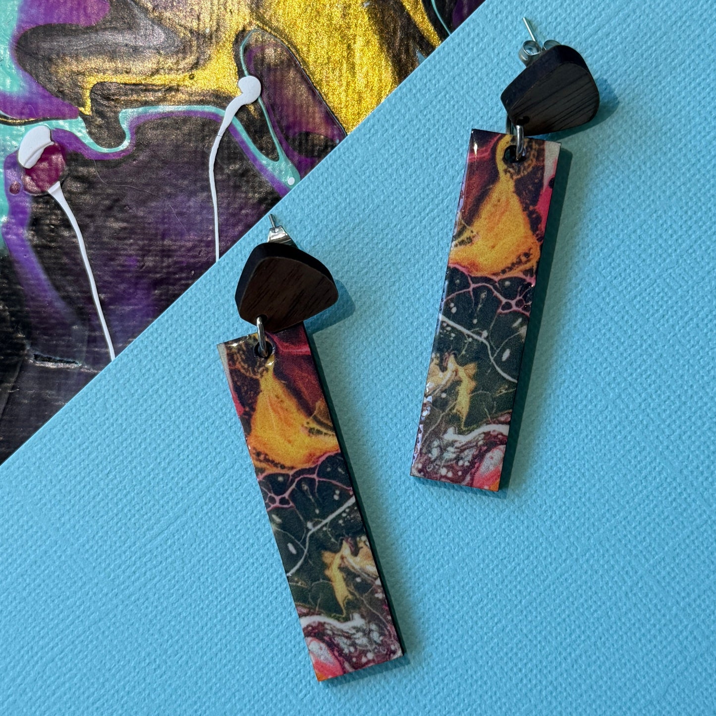 Colorful abstract teardrop earrings with wooden accents on a blue background