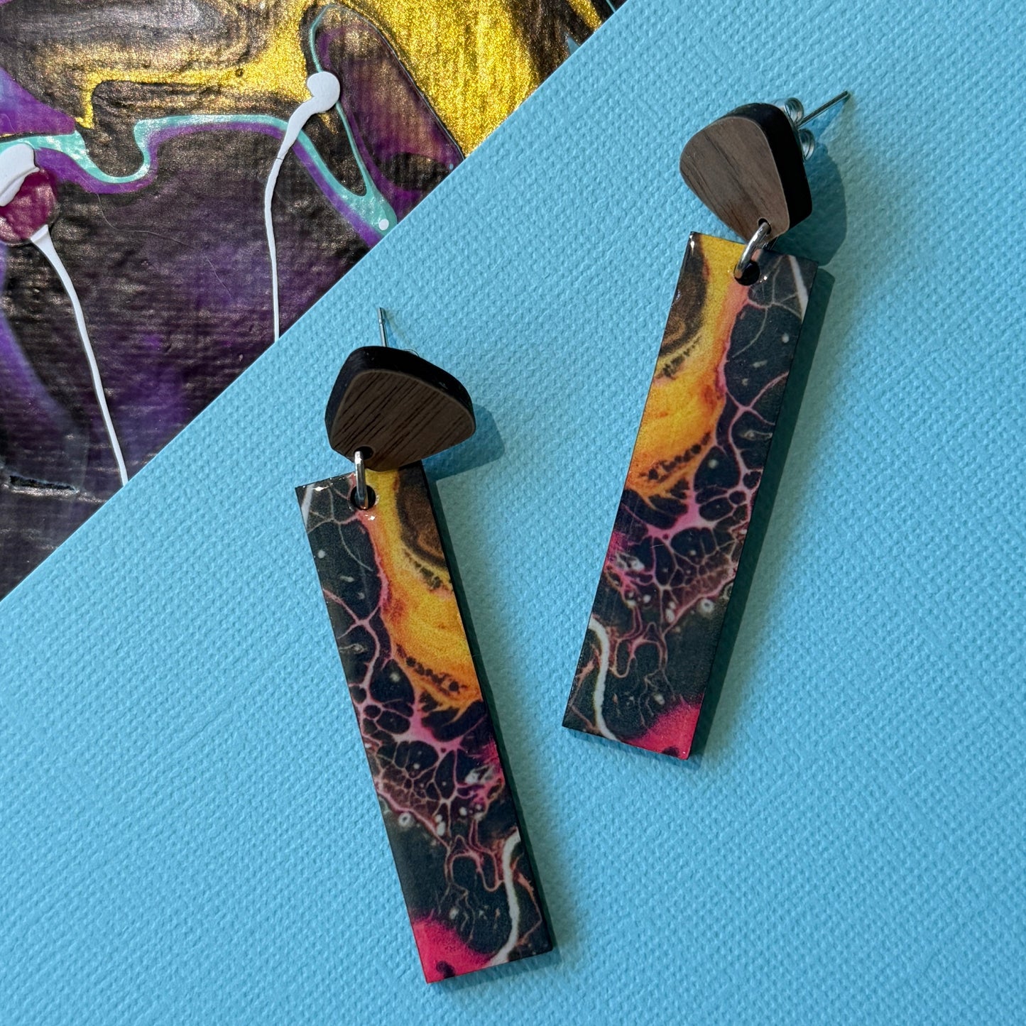 Colorful abstract teardrop earrings with wooden accents on a blue background