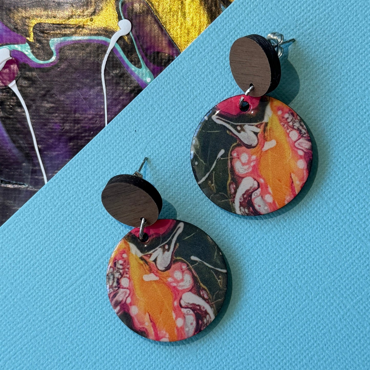 Colorful abstract teardrop earrings with wooden accents on a blue background