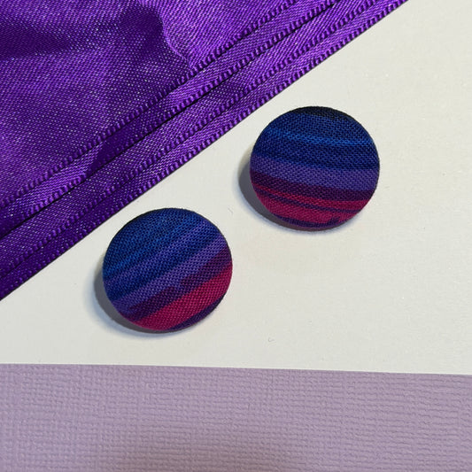 Two round fabric-covered buttons with a striped pattern of navy, purple, and magenta, displayed on a white surface next to a purple zipper.