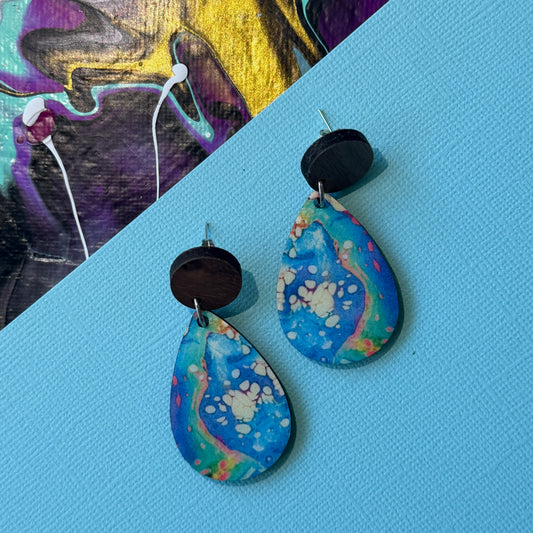 Colorful abstract teardrop earrings with wooden accents on a blue background