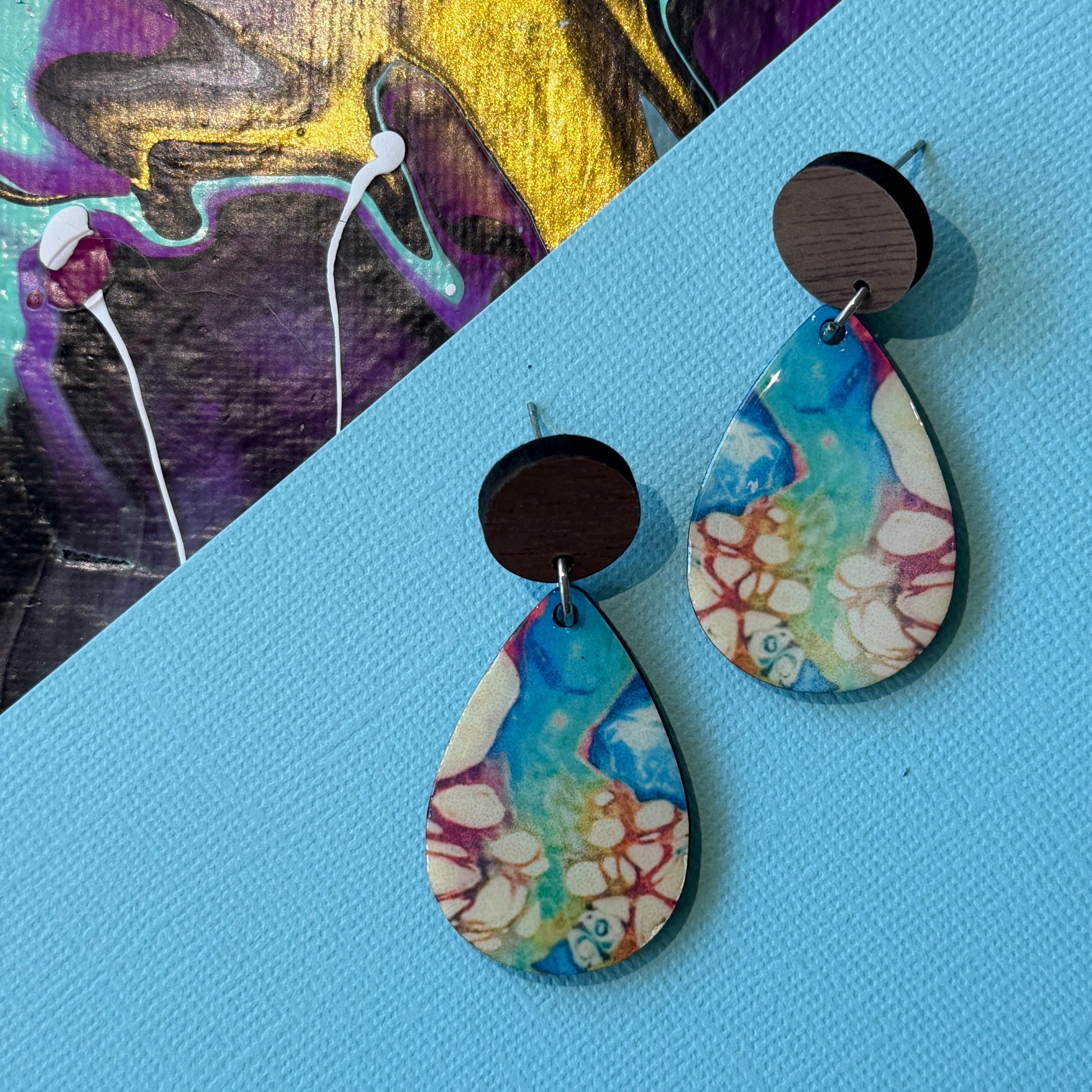 Colorful abstract teardrop earrings with wooden accents on a blue background
