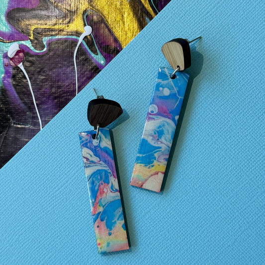Colorful abstract teardrop earrings with wooden accents on a blue background