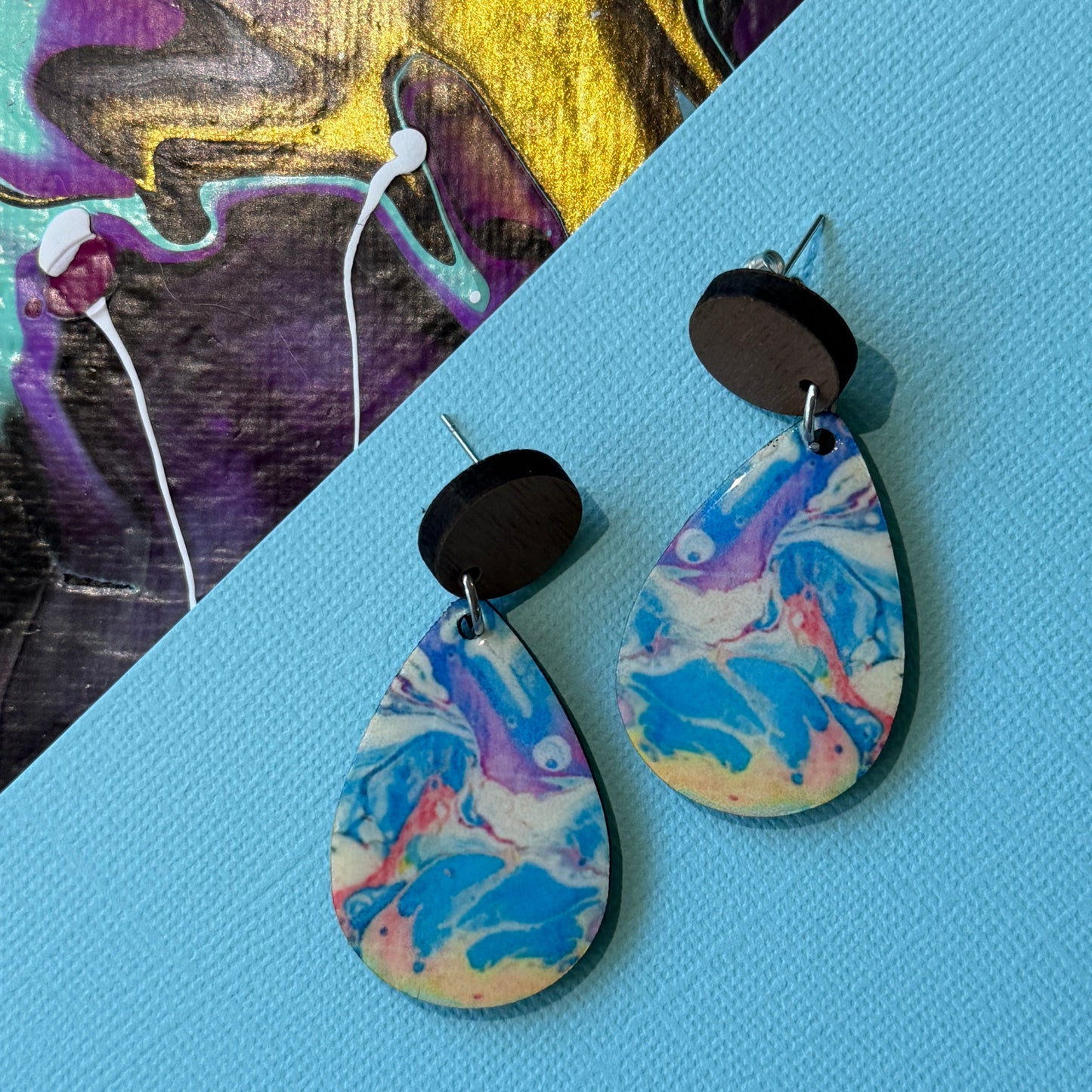 Colorful abstract teardrop earrings with wooden accents on a blue background