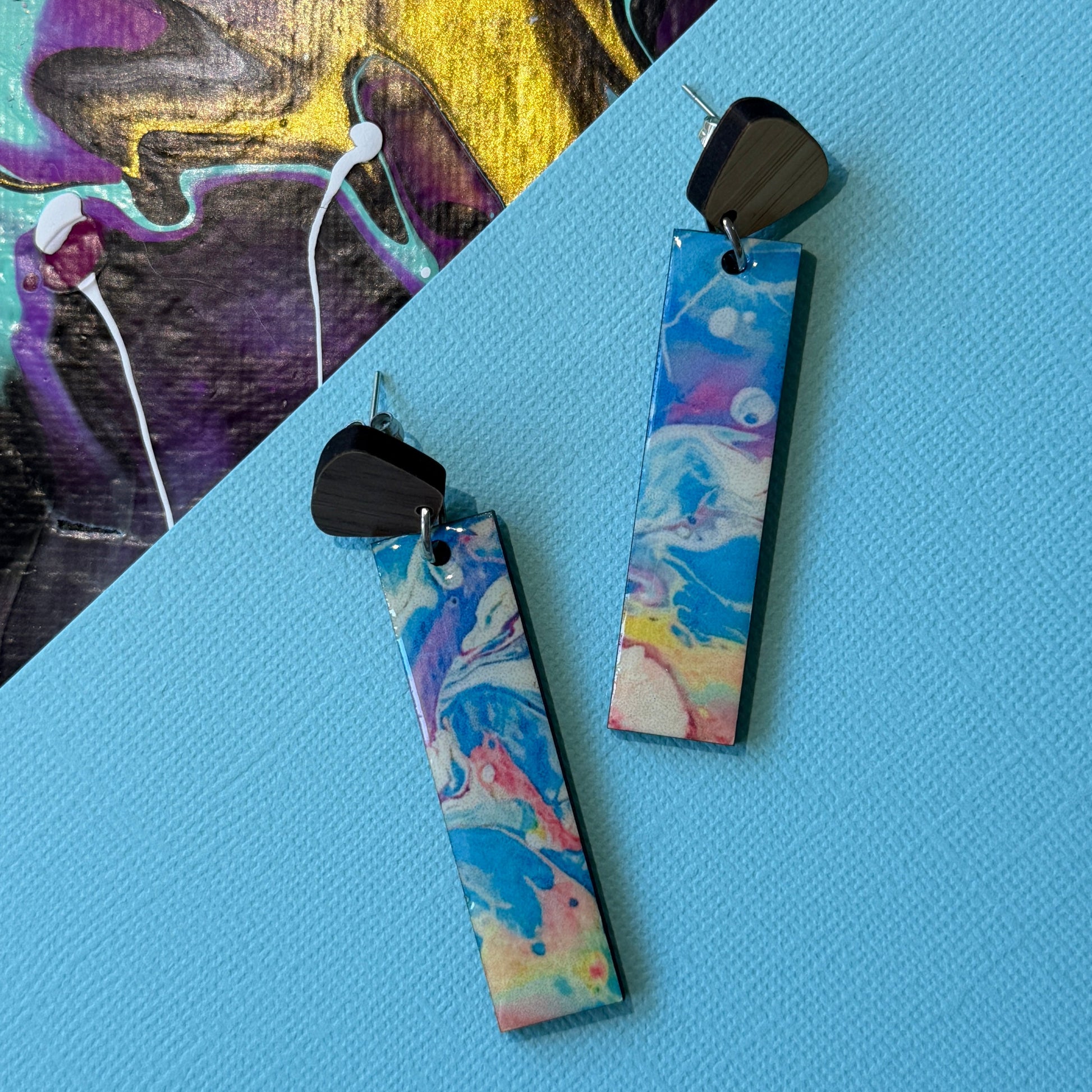 Colorful abstract teardrop earrings with wooden accents on a blue background