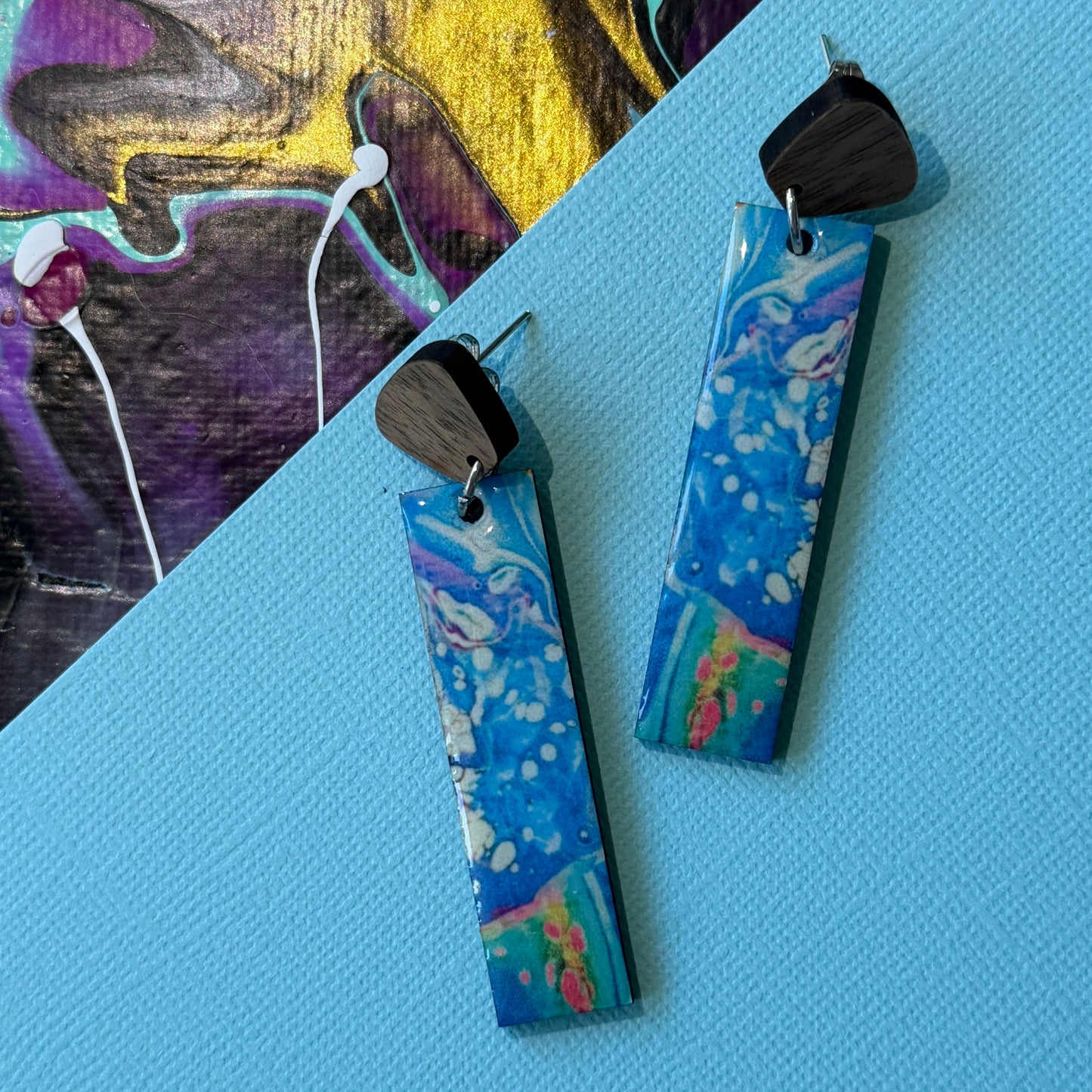 Colorful abstract teardrop earrings with wooden accents on a blue background