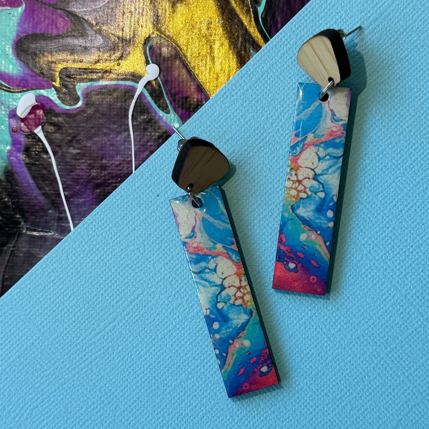 Colorful abstract teardrop earrings with wooden accents on a blue background