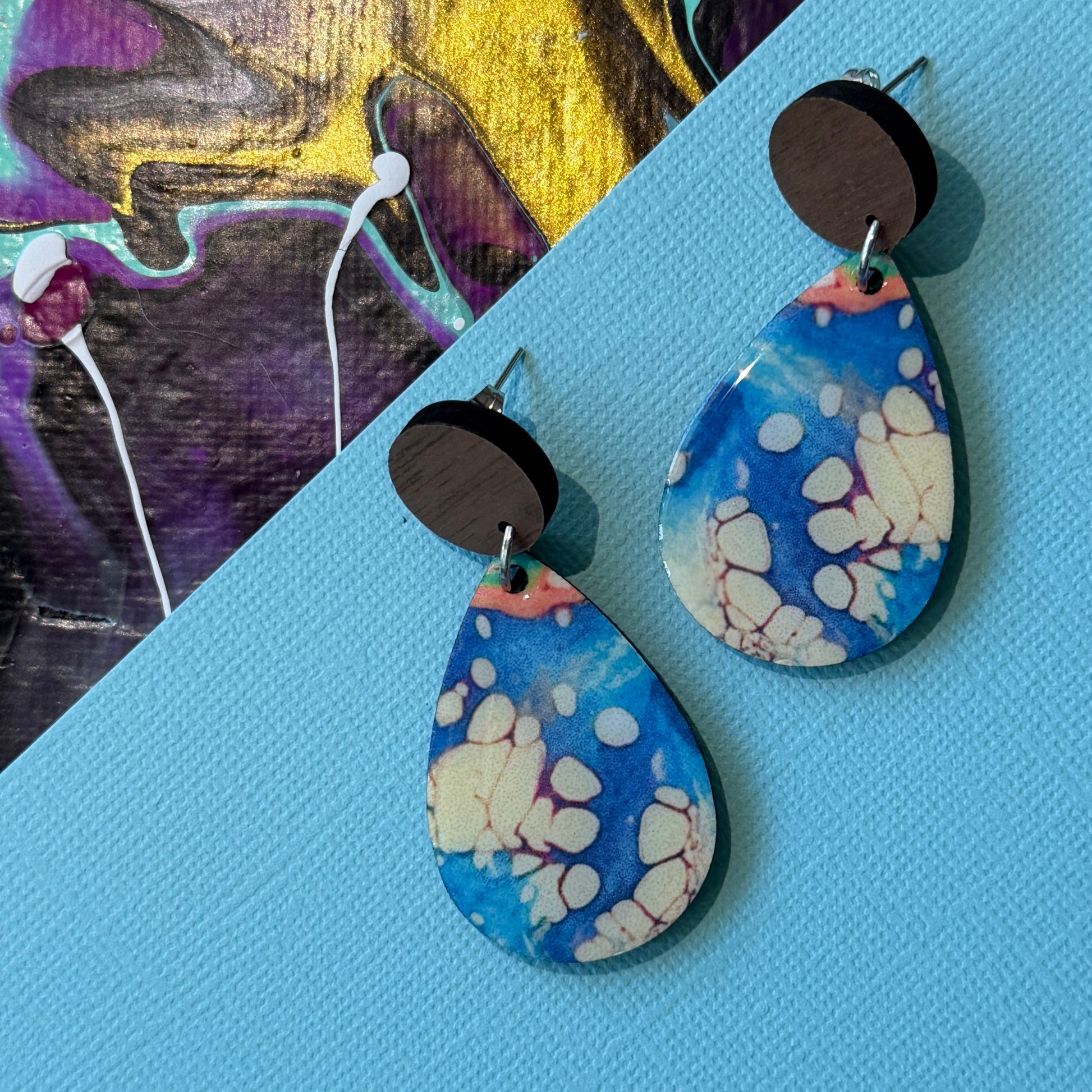 Colorful abstract teardrop earrings with wooden accents on a blue background