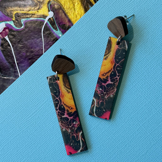 Colorful abstract teardrop earrings with wooden accents on a blue background