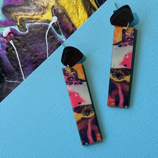 Colorful abstract teardrop earrings with wooden accents on a blue background