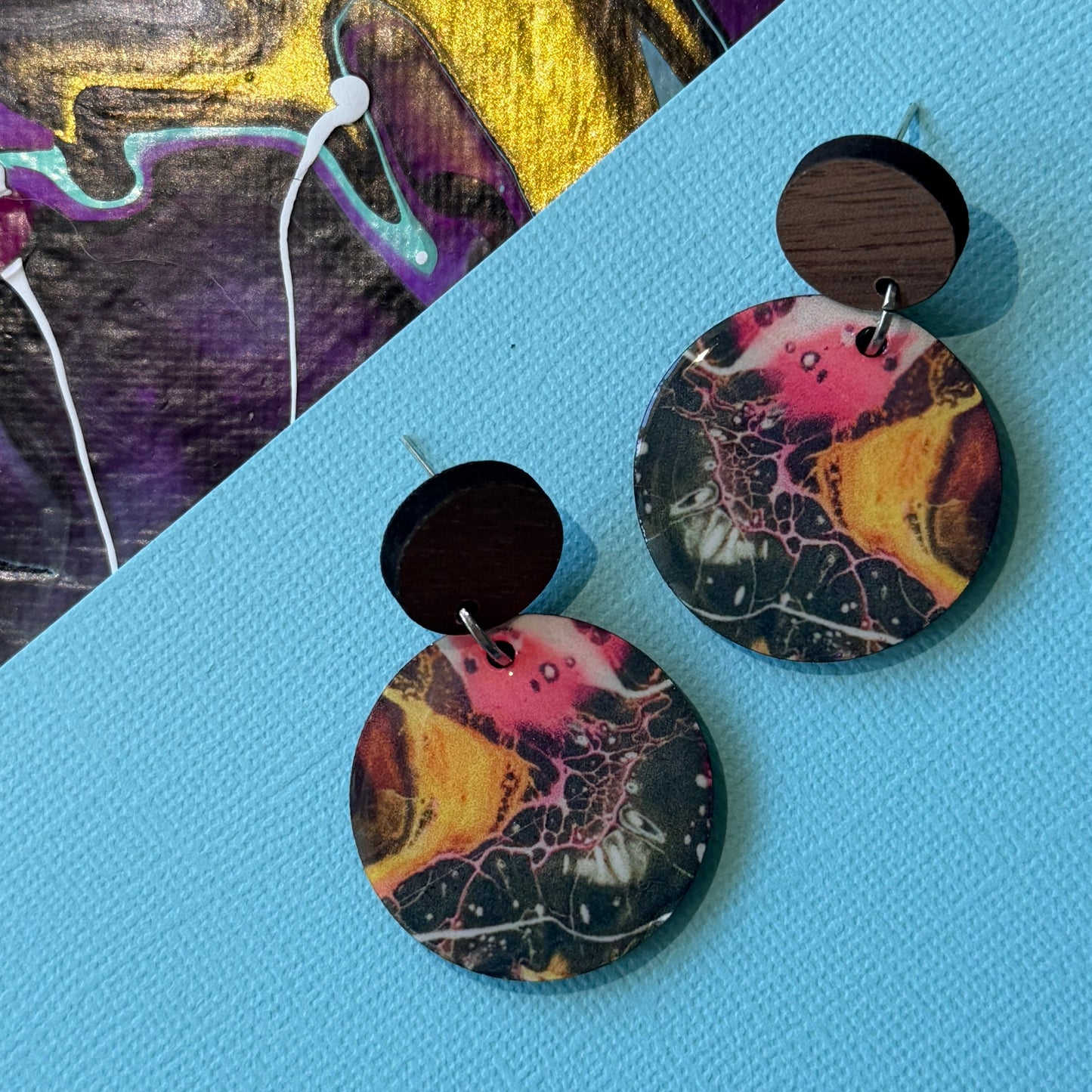 Colorful abstract teardrop earrings with wooden accents on a blue background
