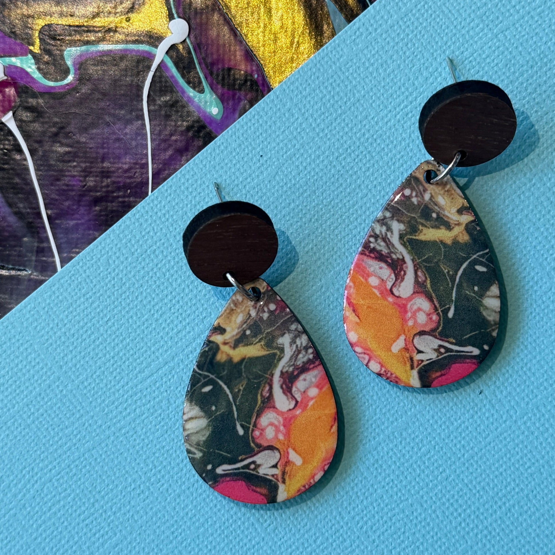 Colorful abstract teardrop earrings with wooden accents on a blue background