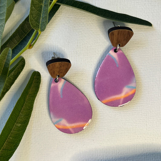 Pair of earrings with purple teardrop-shaped stones on a white fabric background with green leaves.