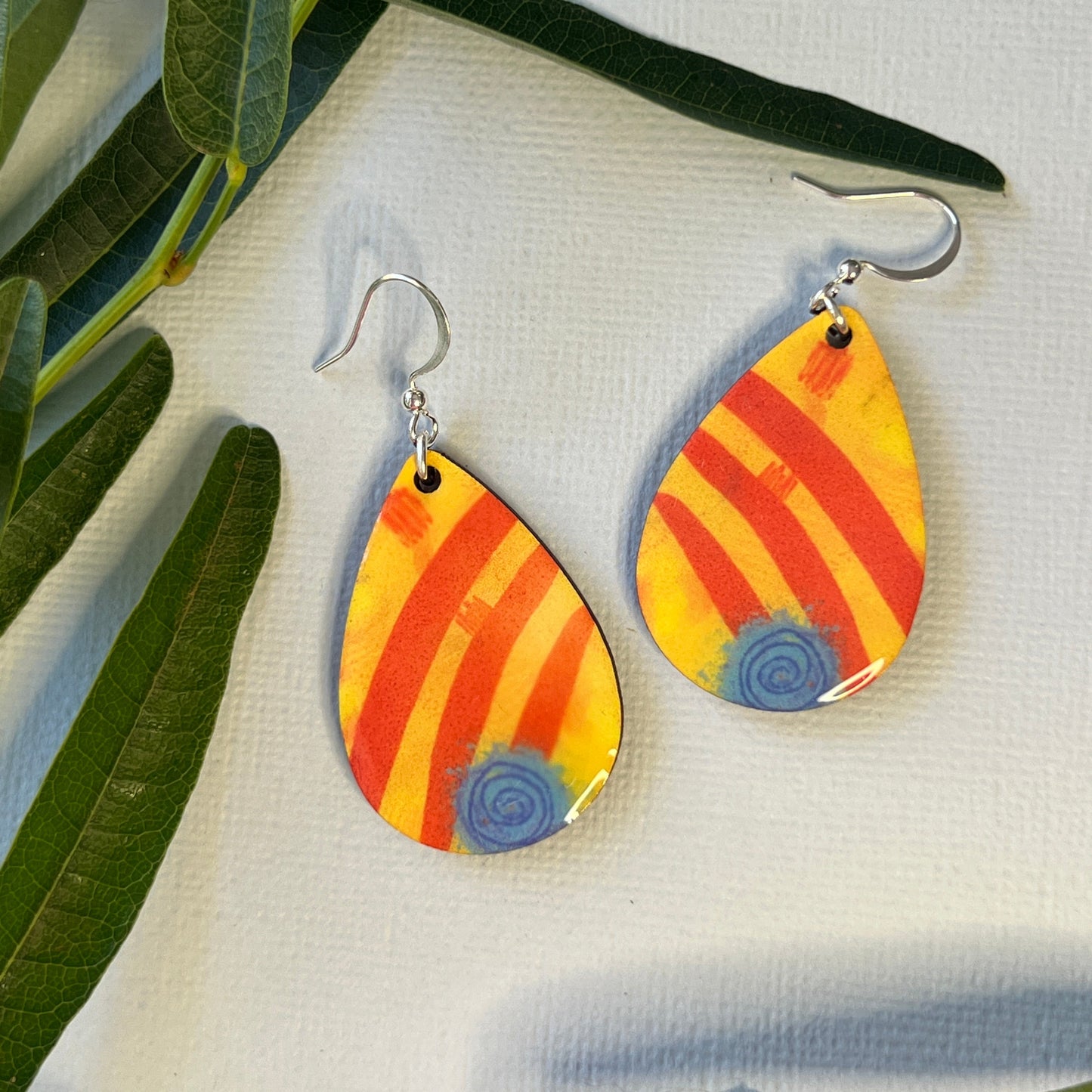 Colorful striped earrings on a white fabric background with green leaves.