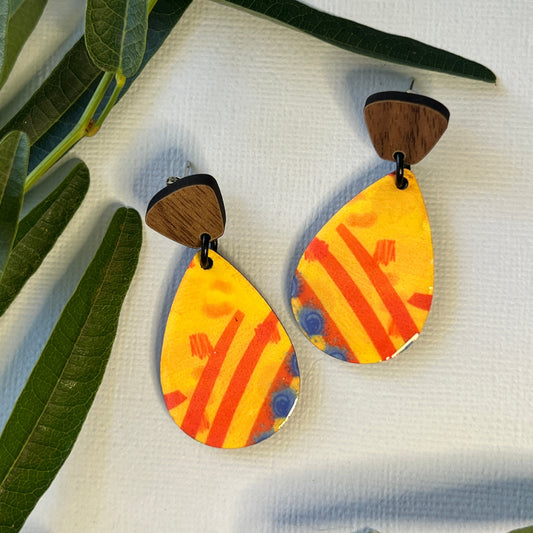 Colorful abstract-patterned earrings on a white fabric background with green leaves.