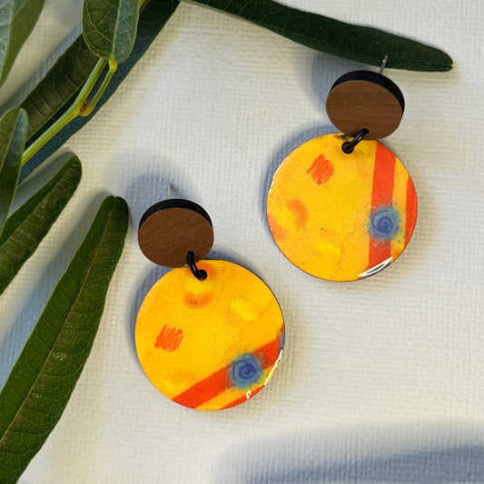 Pair of round earrings with a colorful design on a white background with green leaves.