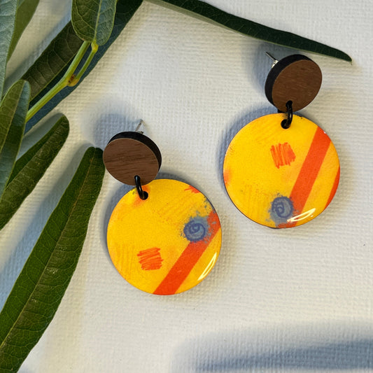 Colorful circular earrings with wooden accents on a textured surface with leaves in the foreground