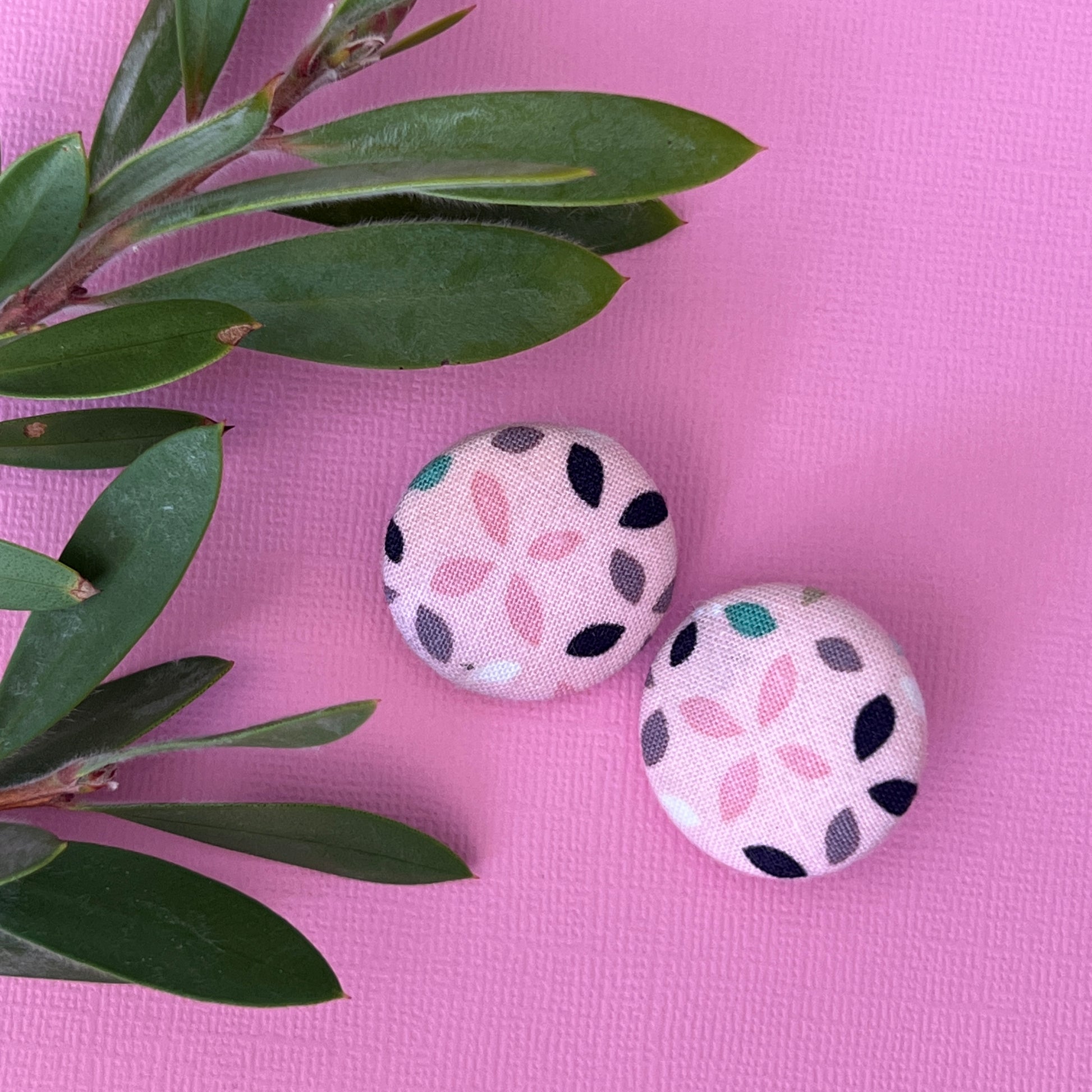 Two decorative buttons with floral pattern on a pink background with green leaves.