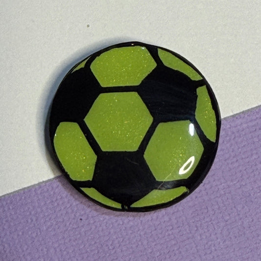 Green and Black soccer ball magnet. On white and purple background.