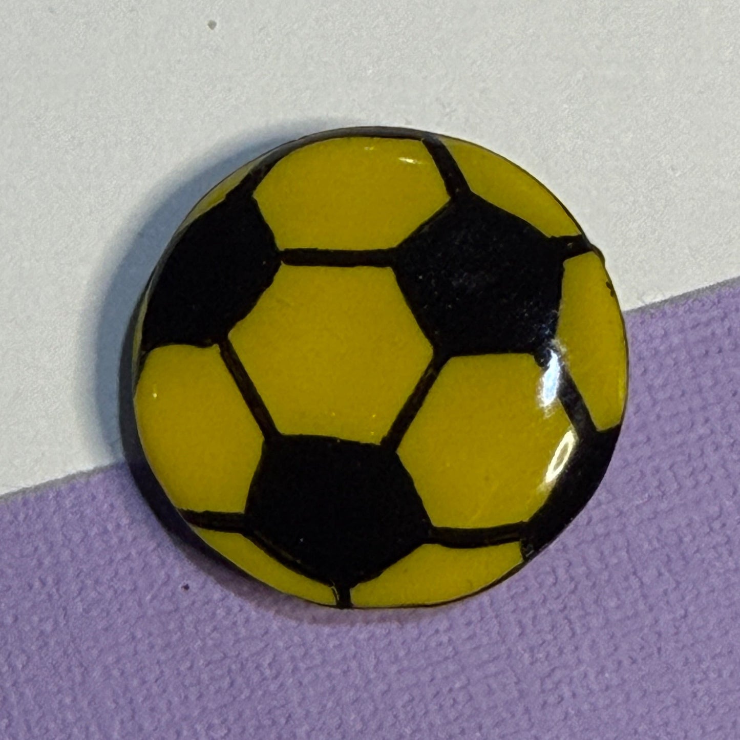 Yellow and black soccer ball magnet. On White and Purple background