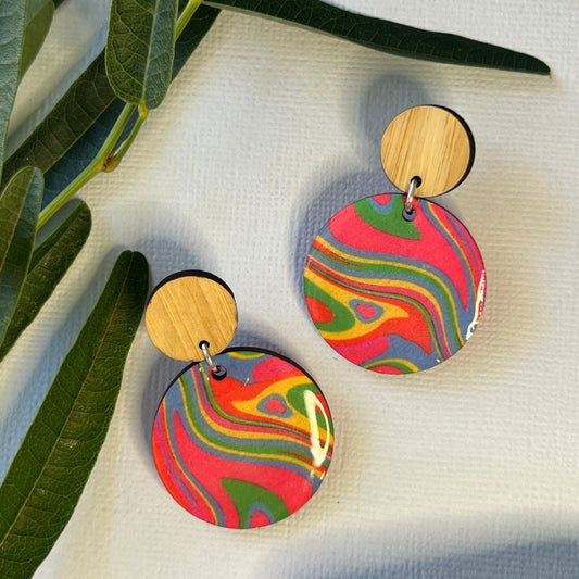 Colorful round earrings on a textured surface with green leaves in the foreground